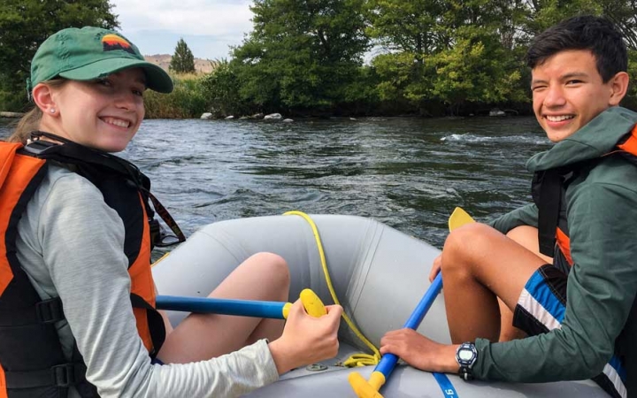 two young people sitting at the front of a raft look back at the camera and smile
